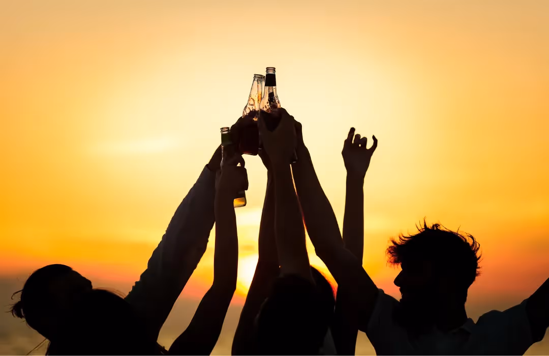 Silhouetted group of friends raising their drinks in a celebratory toast against a golden sunset. A vibrant HOMETAINMENT experience in London, perfect for private parties, bespoke home gatherings, and exclusive outdoor events.