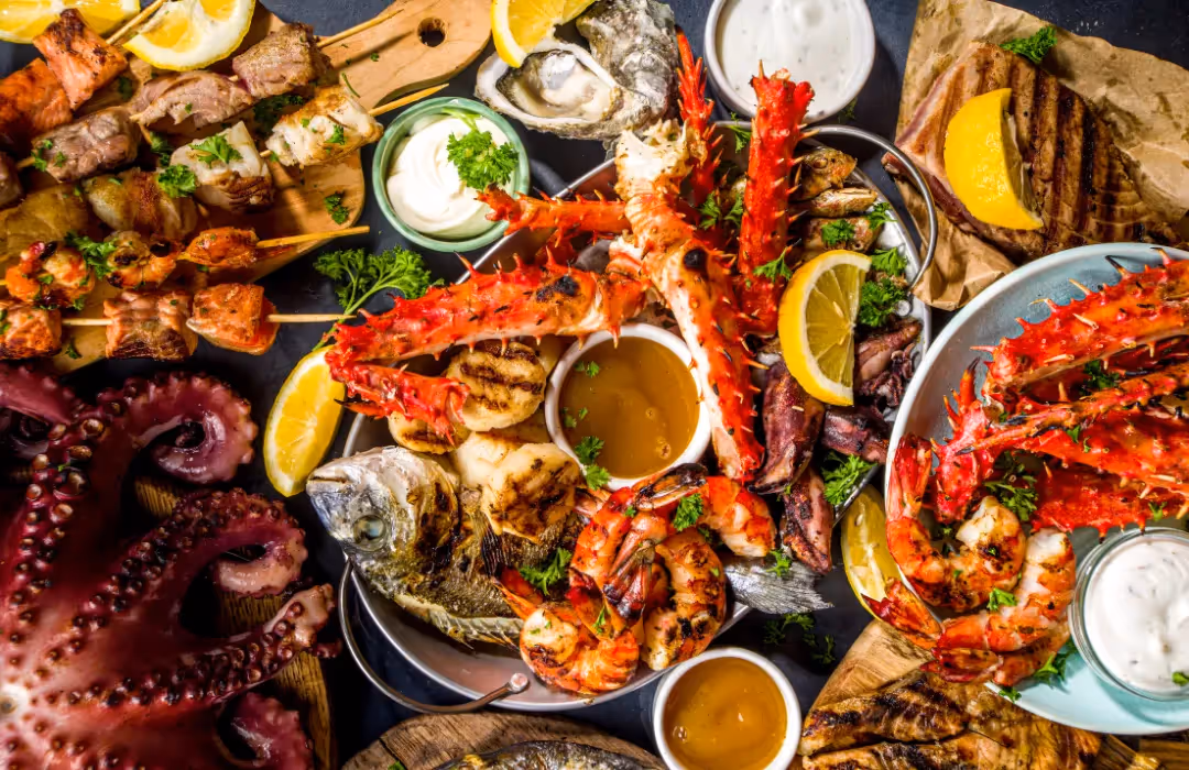 A luxurious seafood feast featuring grilled prawns, king crab legs, oysters, octopus, and skewered fish, served with fresh lemon, sauces, and herbs. A premium HOMETAINMENT dining experience in London, perfect for private chef services and exclusive home events.