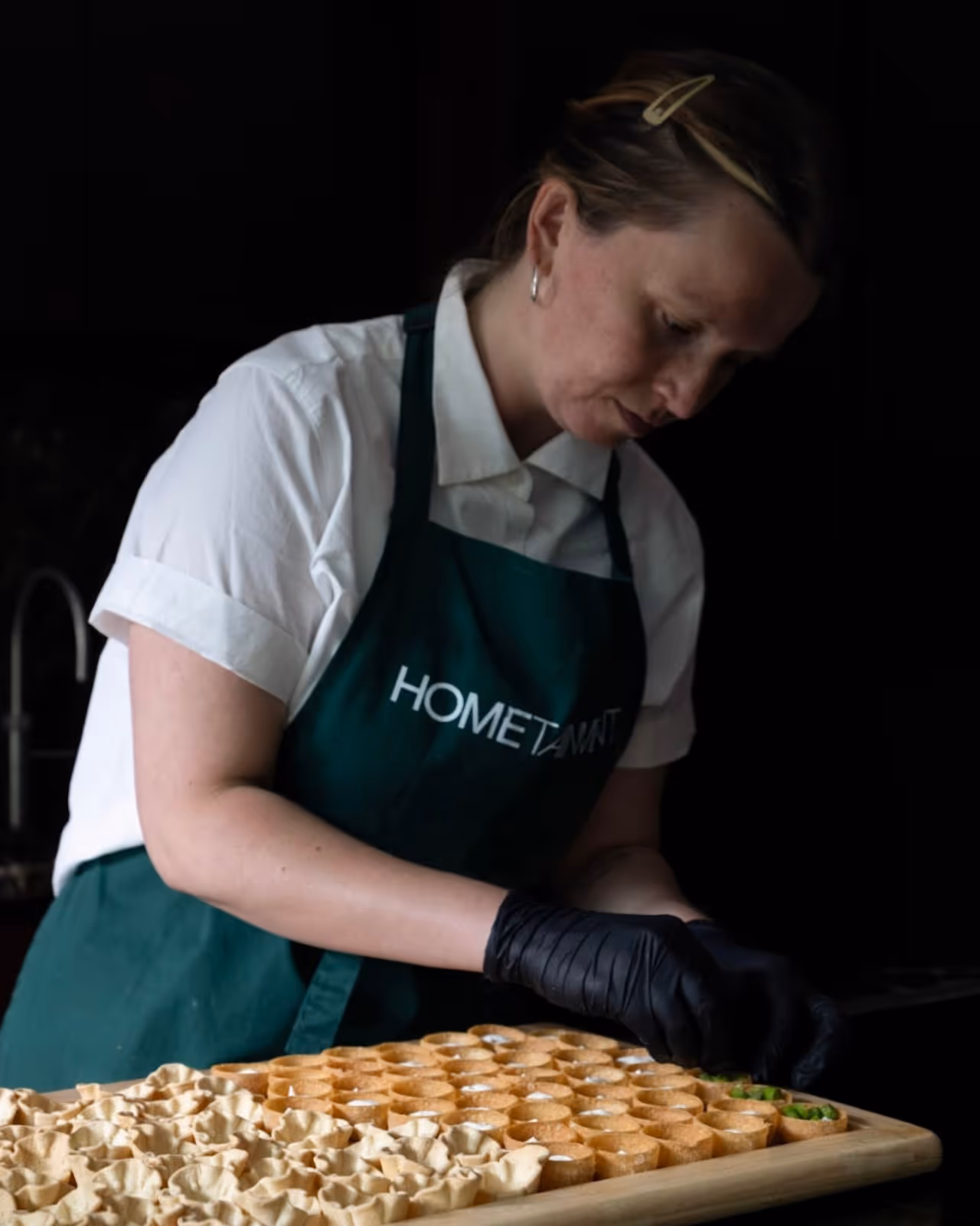 Private chef preparing canapé bites by hand in a luxury kitchen while wearing a HOMETAINMENT apron, showcasing fine dining catering for private events in London