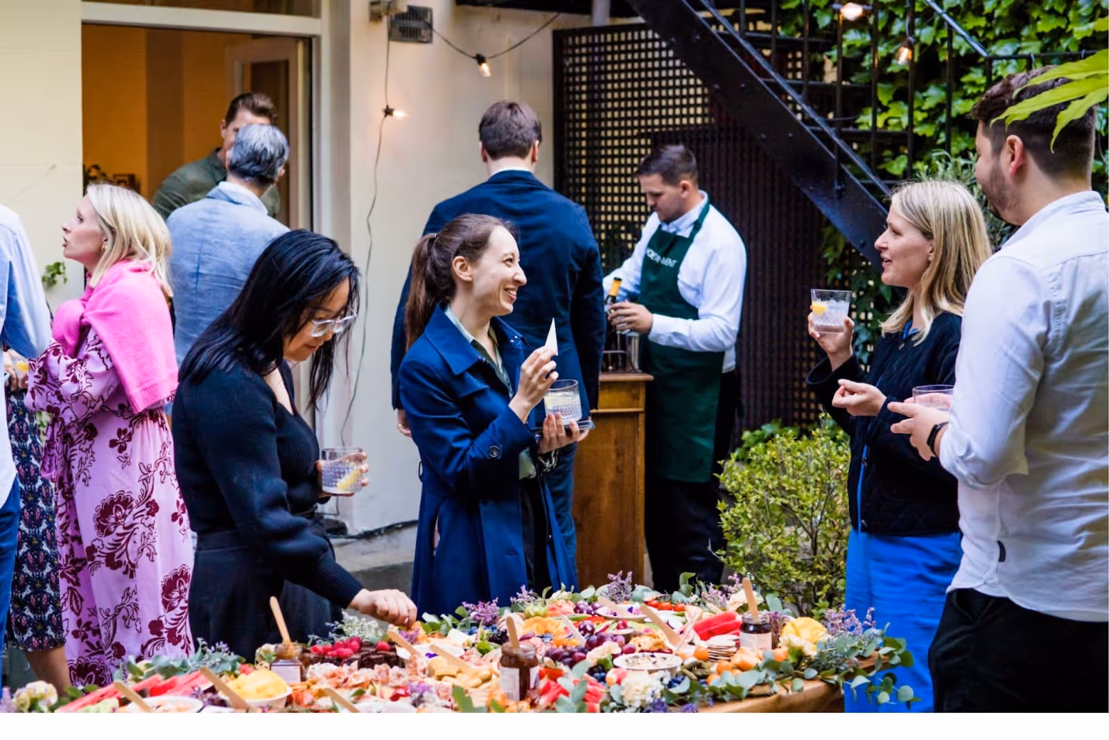 People gathered around a grazing board table chatting and socialising while drinking in a garden in London..
