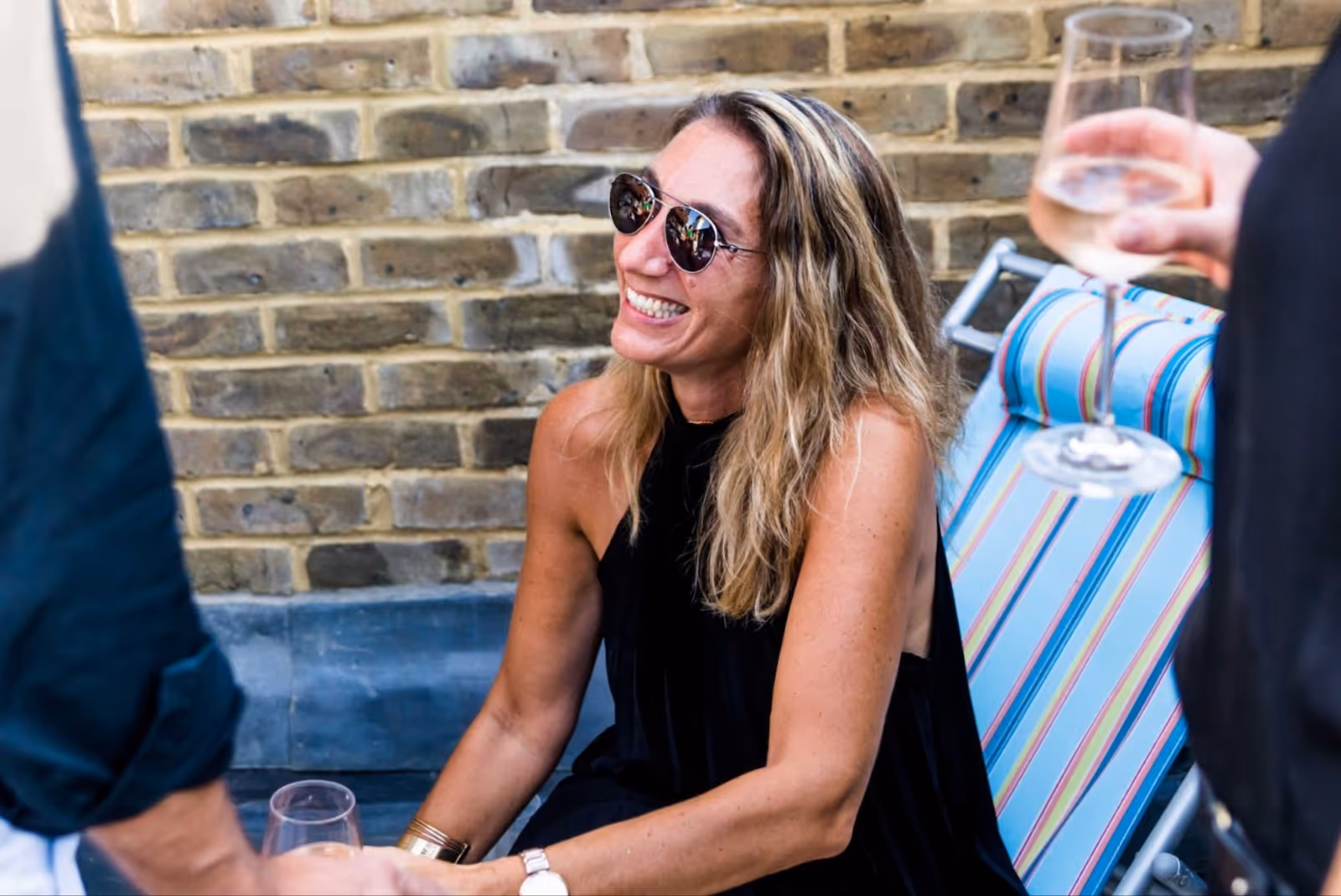 Pretty blond woman sitting down at a busy summer party on a sun chair. 