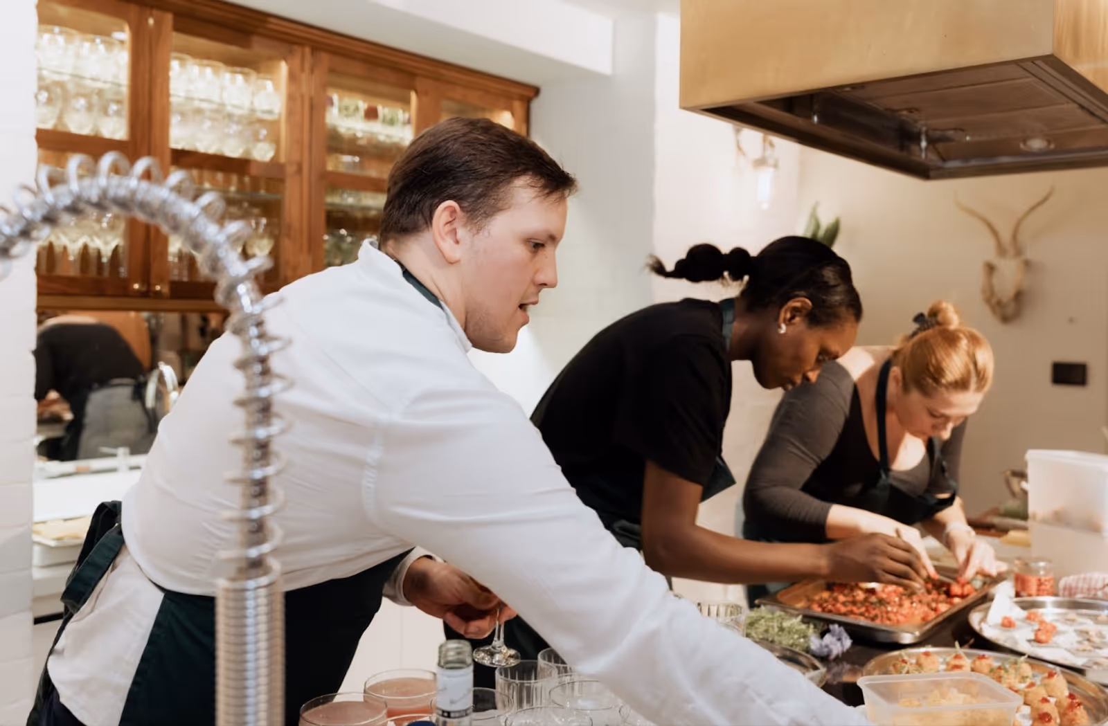 Three chefs in a bright clean kitchen, cooking all together, working on details of food presentationl.