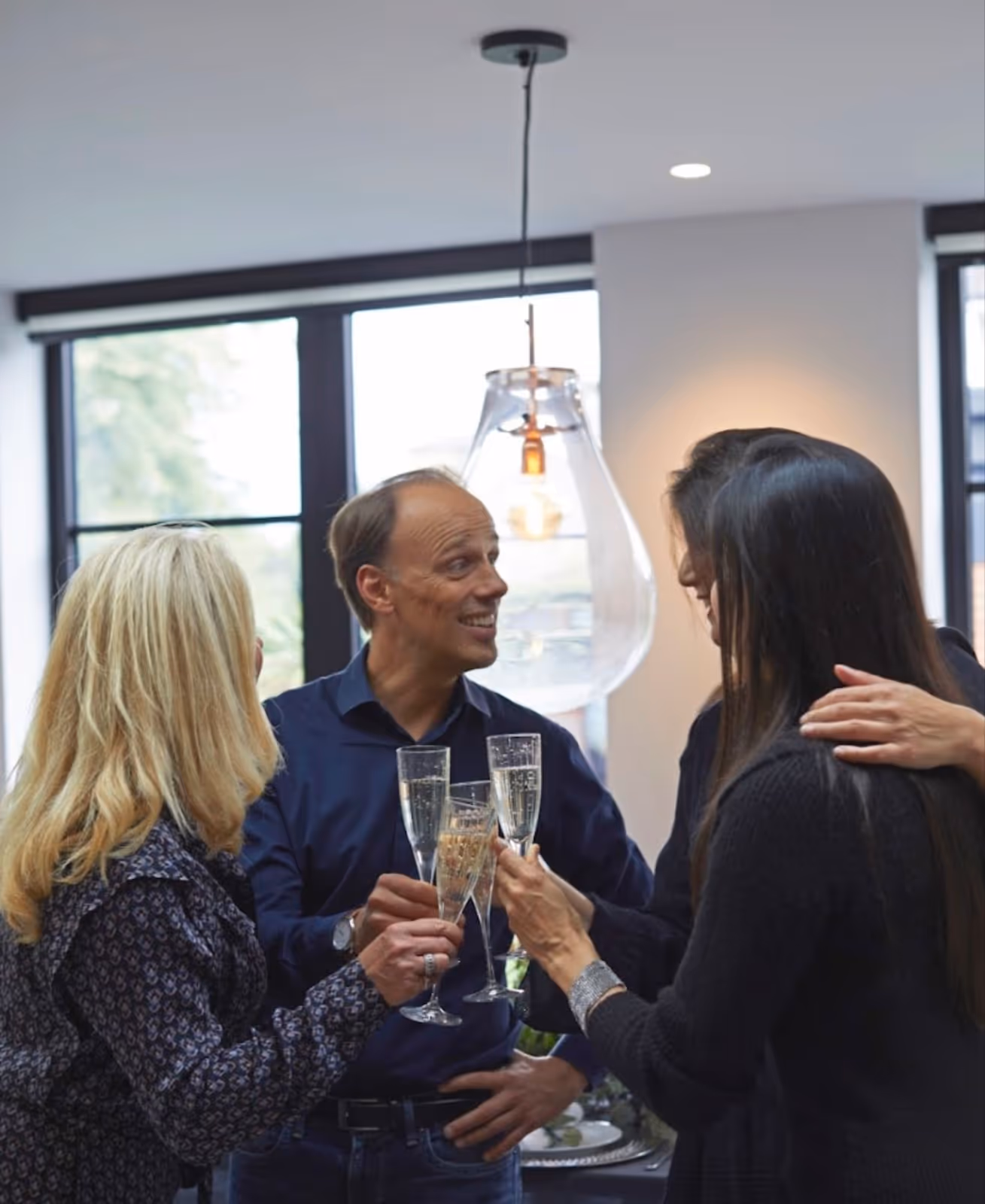 People gathered around, holding a glass of champagne and laughing inside a modern London home.