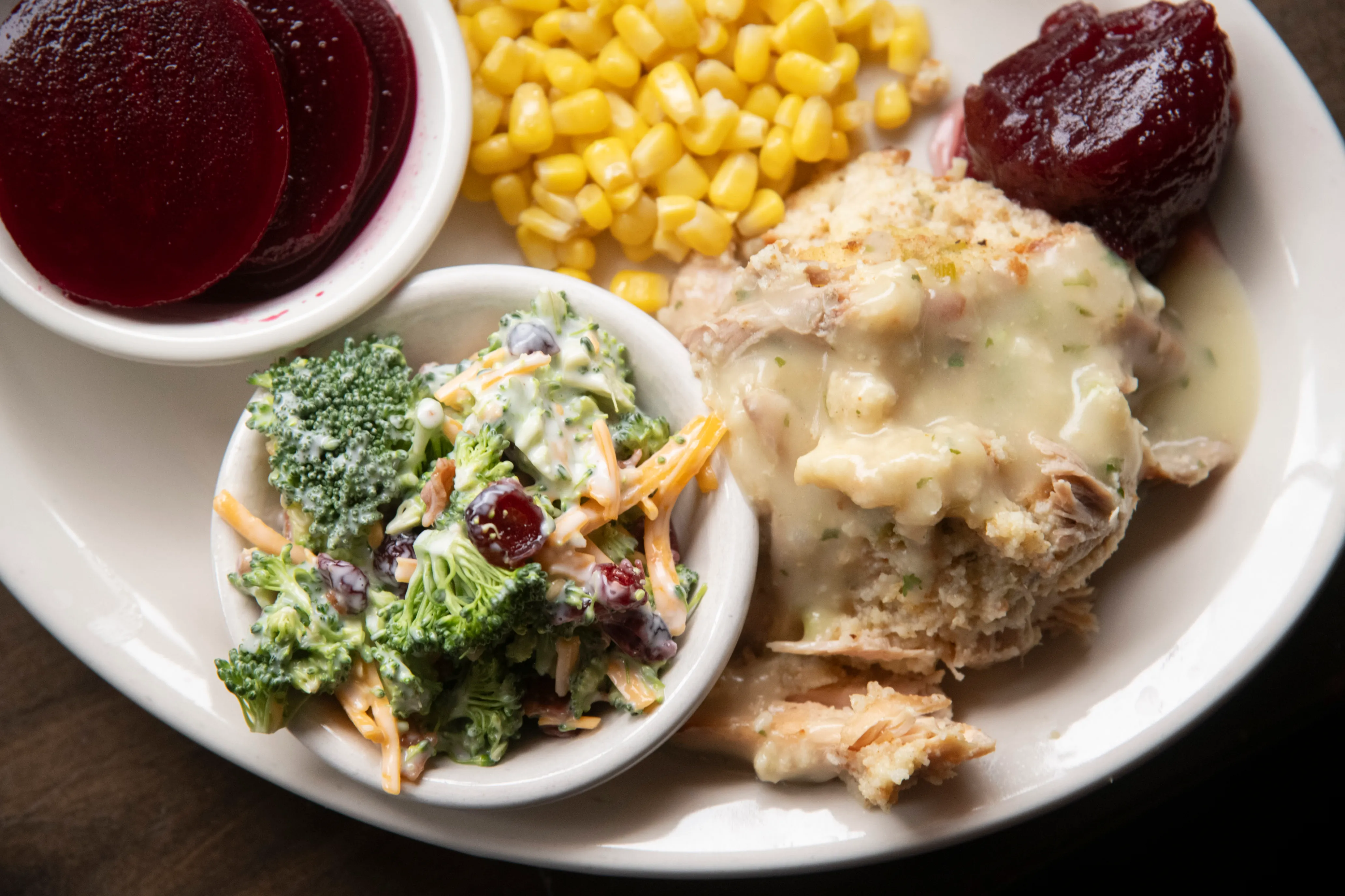 Plate with corn, cranberry sauce, broccoli salad with cheese and cranberries, and turkey topped with creamy gravy.