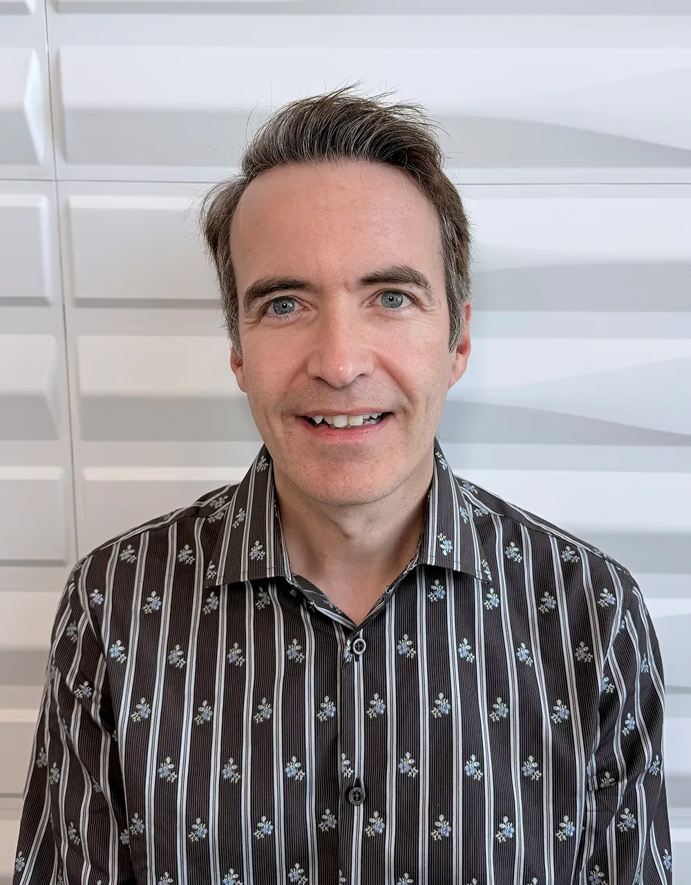 A profile picture of Dr. Duane Hartley in front of a white wall with a raised wave pattern.