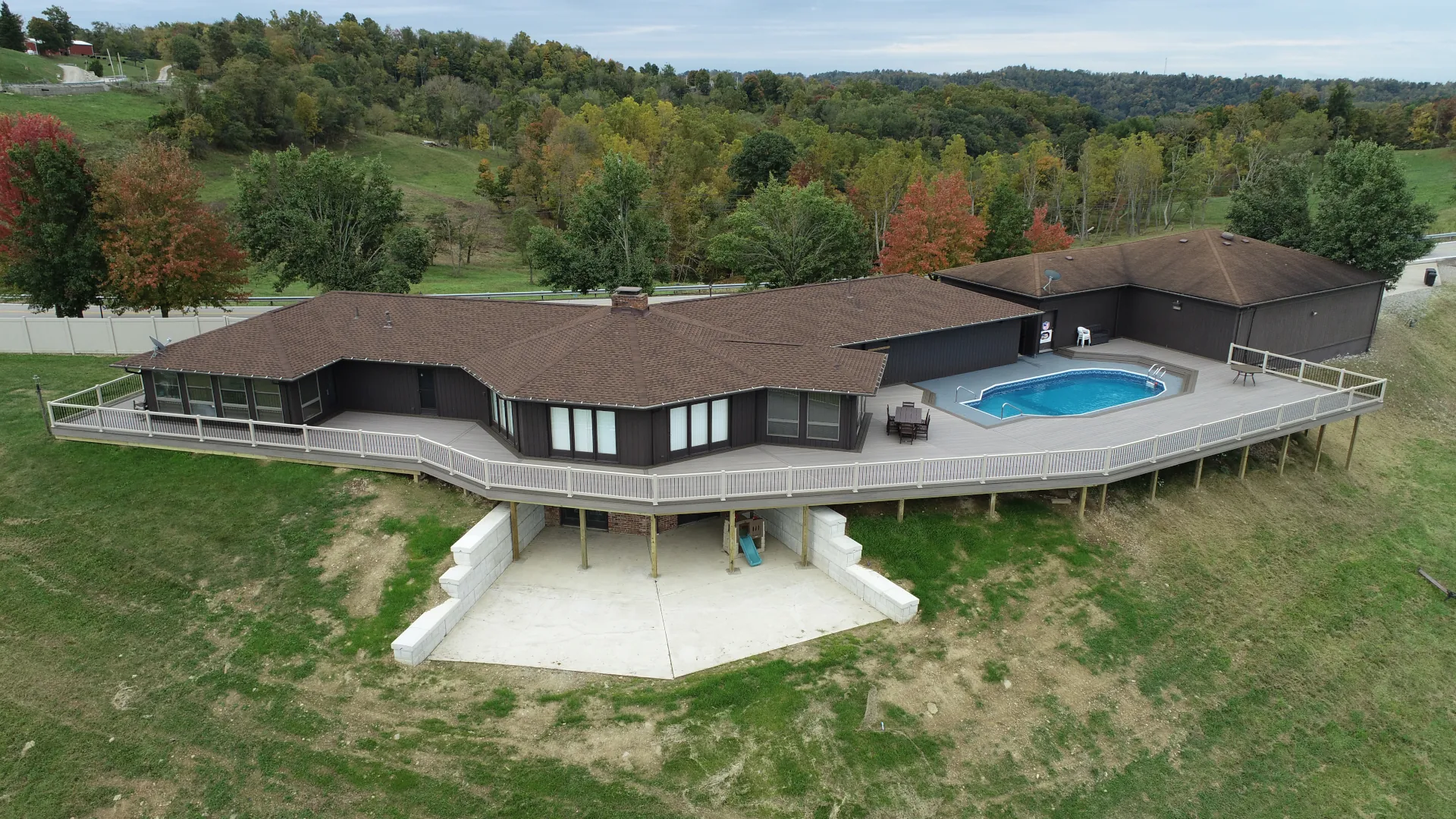 Aerial view of a large elevated composite deck surrounding a backyard pool with white railings and views of a wooded hillside.