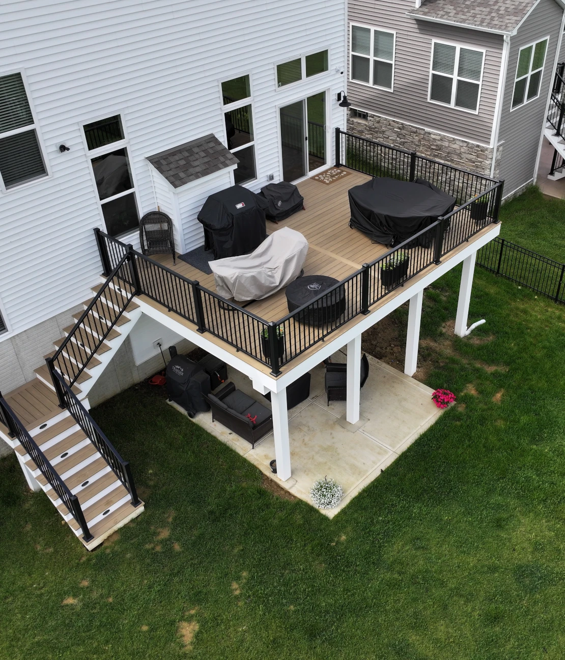 Angled aerial view of a Weathered Teak elevated deck with black aluminum railing, white fascia, and covered patio space below in Plain City, Ohio.