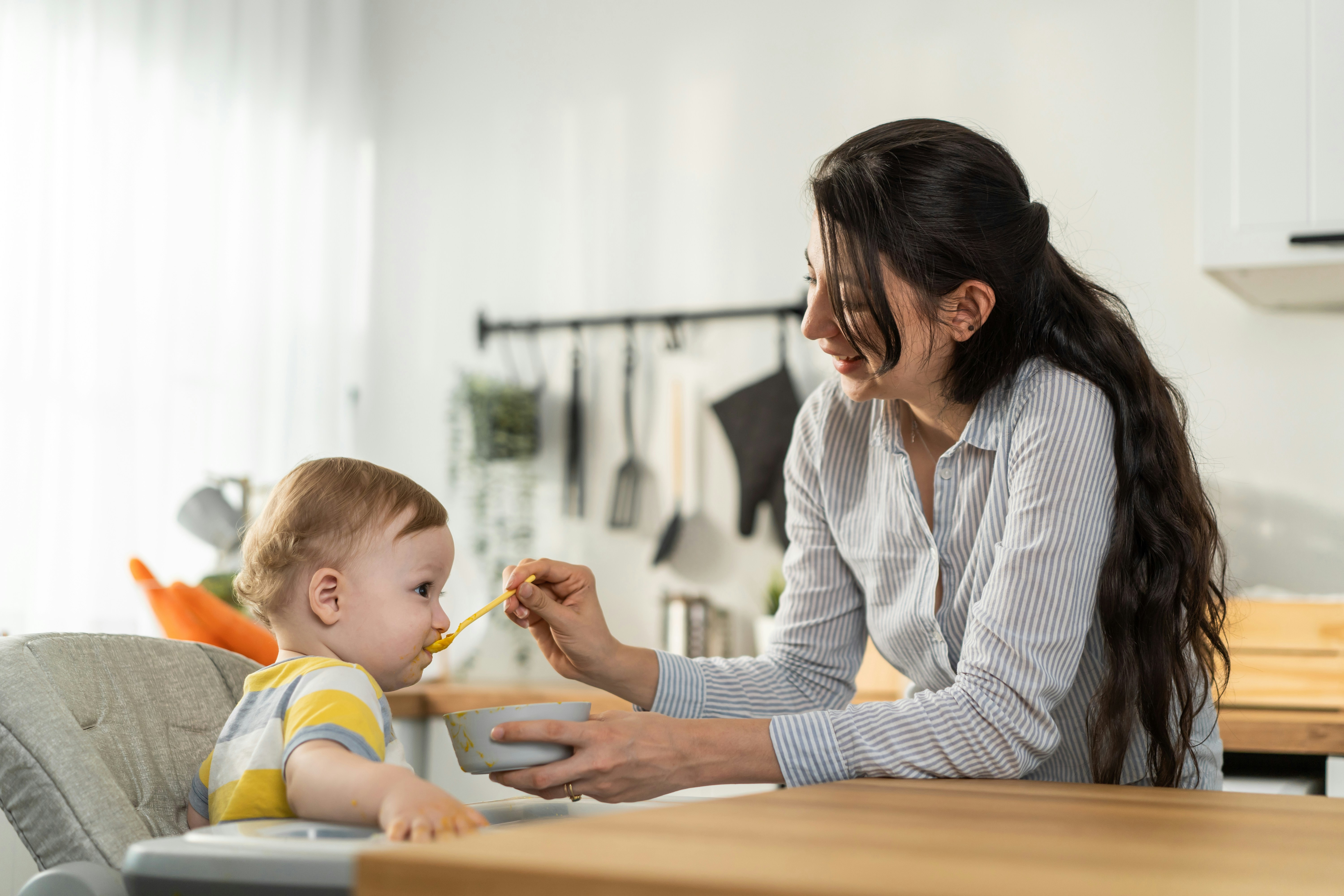 Caregiver feeding a young child during a calm daily routine, demonstrating patience, care, and consistent support that helps children feel safe and understood.