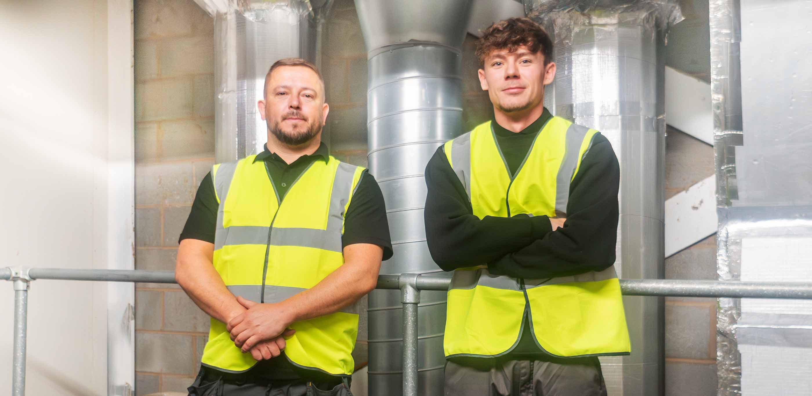 Two men in high-viz jackets standing in front of metal pipes