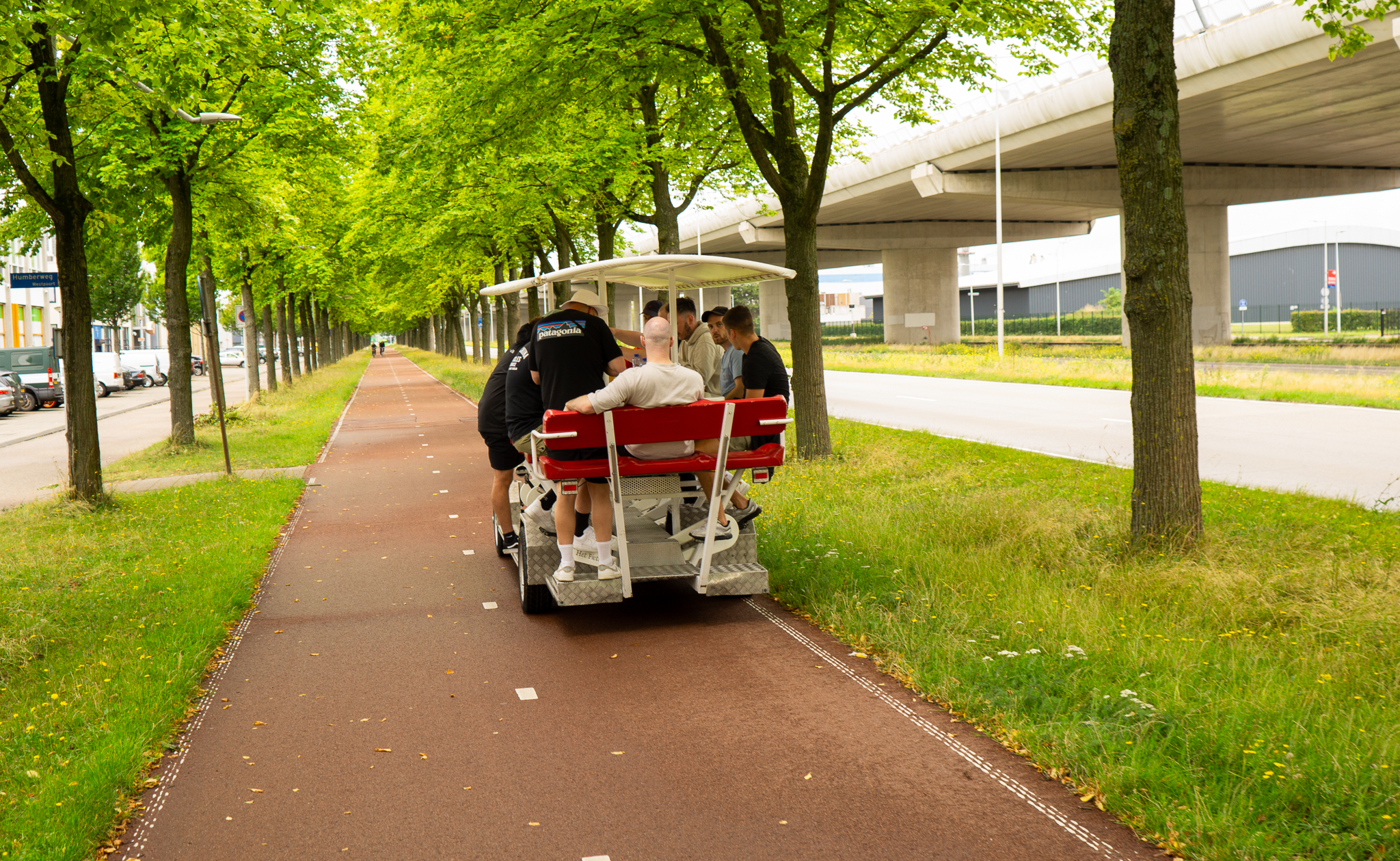 Group of people riding a pedal-powered party bike with a canopy on a tree-lined bike path.