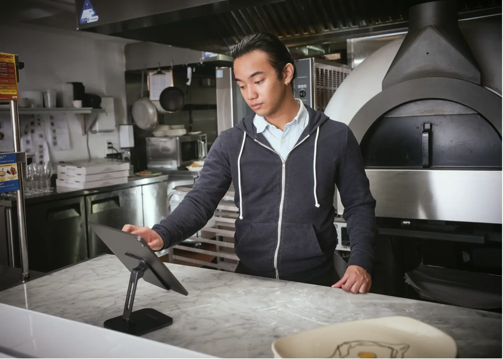 A kitchen staff member operates the MenuSifu POS tablet to view and manage incoming restaurant orders.