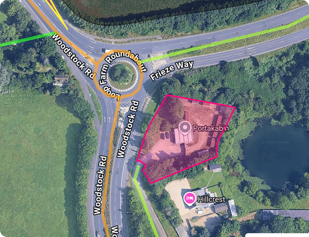 Aerial view of the Loop Farm Roundabout on Woodstock Road near Frieze Way, showing the Portakabin site and nearby Hillcrest building surrounded by greenery and a pond.