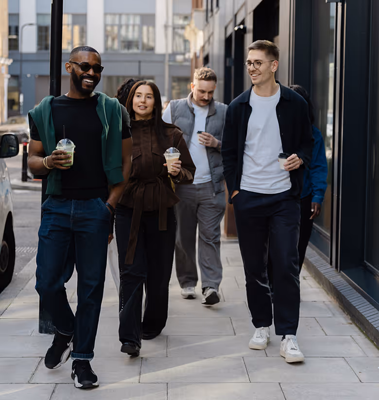 A group of five coworkers in an office celebrating a birthday with a chocolate cake with lit candles and a gift box.