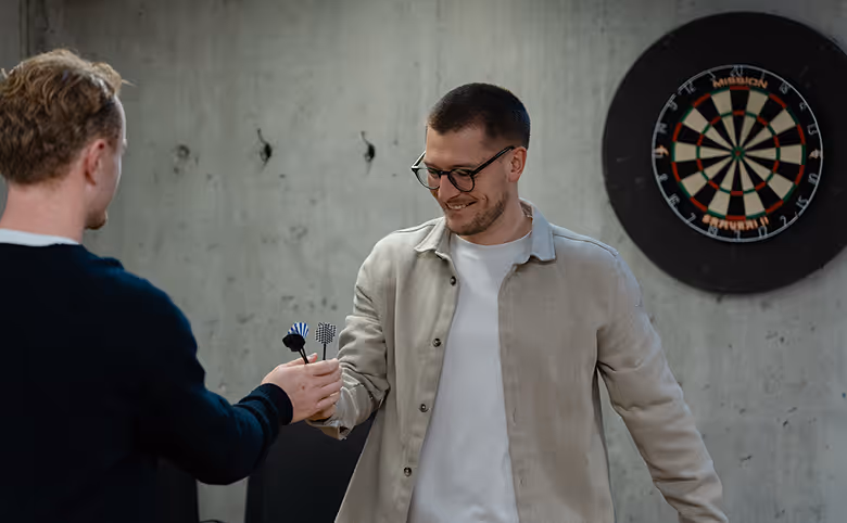 A group of five coworkers in an office celebrating a birthday with a chocolate cake with lit candles and a gift box.