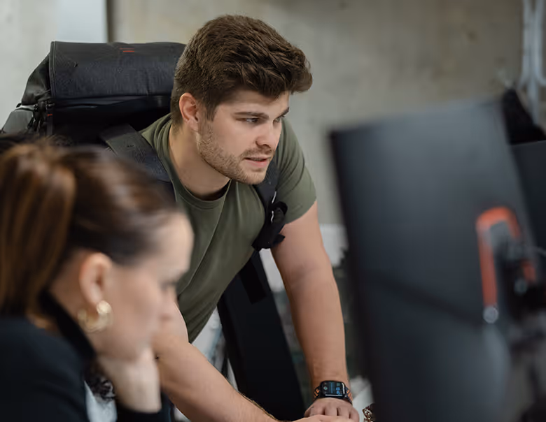 A group of five coworkers in an office celebrating a birthday with a chocolate cake with lit candles and a gift box.