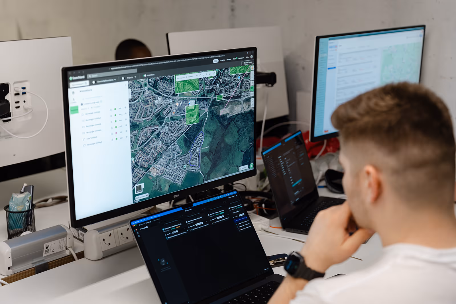 Man analysing a satellite map and data on multiple computer screens in an office.