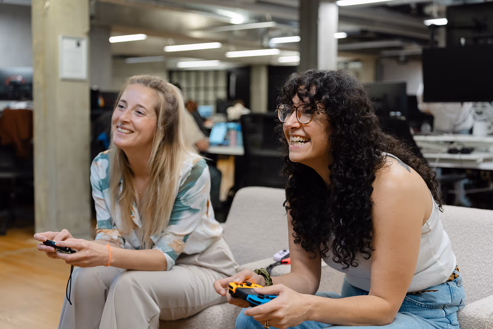 A group of five coworkers in an office celebrating a birthday with a chocolate cake with lit candles and a gift box.