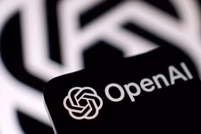 Close-up of the OpenAI logo and text on a black surface with a blurred larger OpenAI logo in the background.