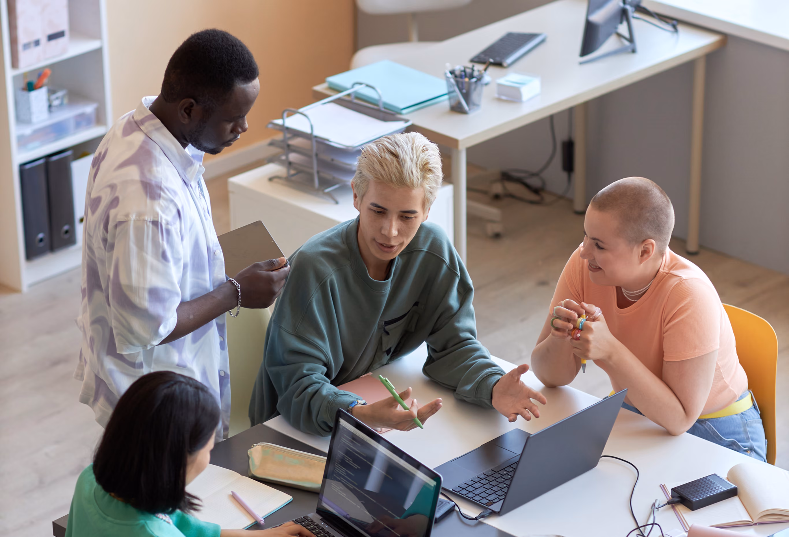 Four diverse coworkers engaged in a discussion around a white table with laptops and notebooks in a modern office.