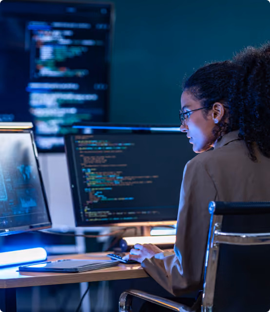 Engineer reviewing code on multiple monitors in a dark office