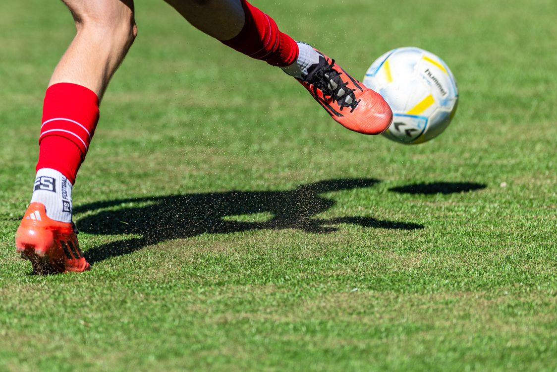A soccer player kicks a ball across a green field during a game, captured in mid-action.