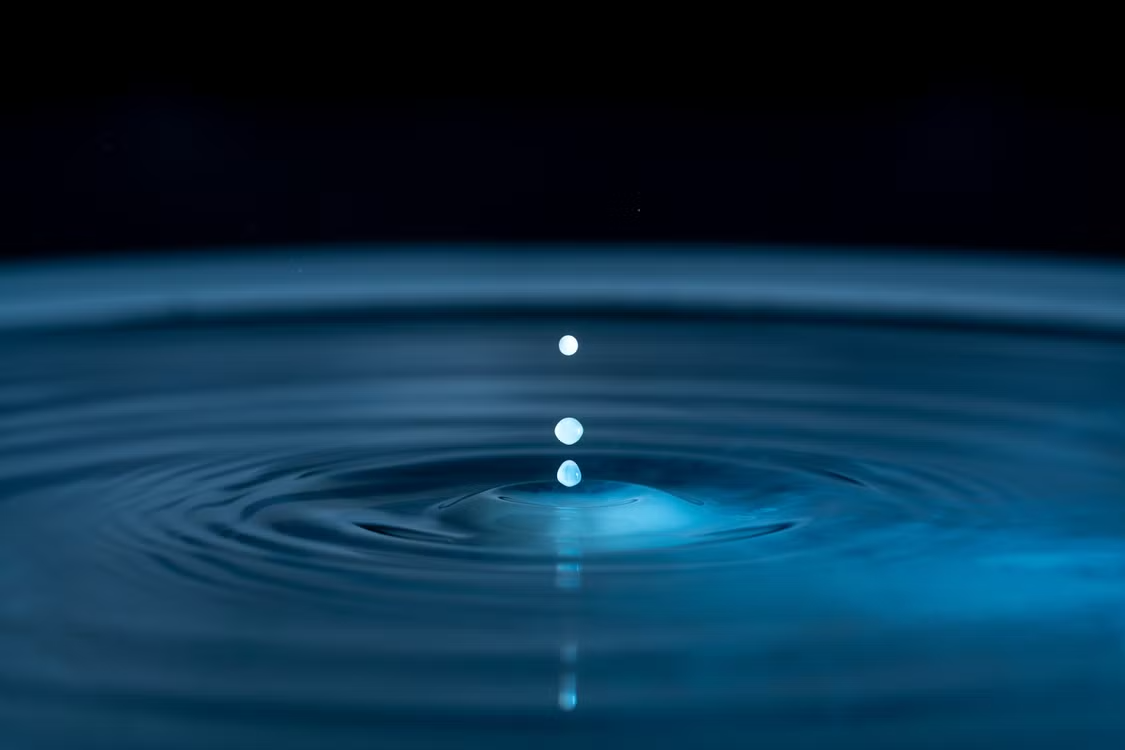Close-up of water droplets creating ripples on a blue water surface.