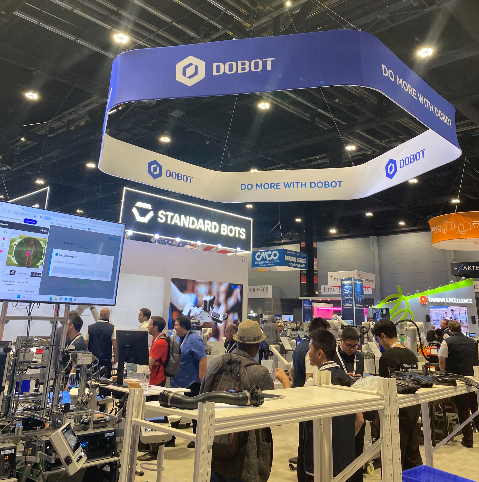 Overhead DOBOT booth signage at Automate 2026 with attendees exploring robotics and automation exhibits on the trade show floor.
