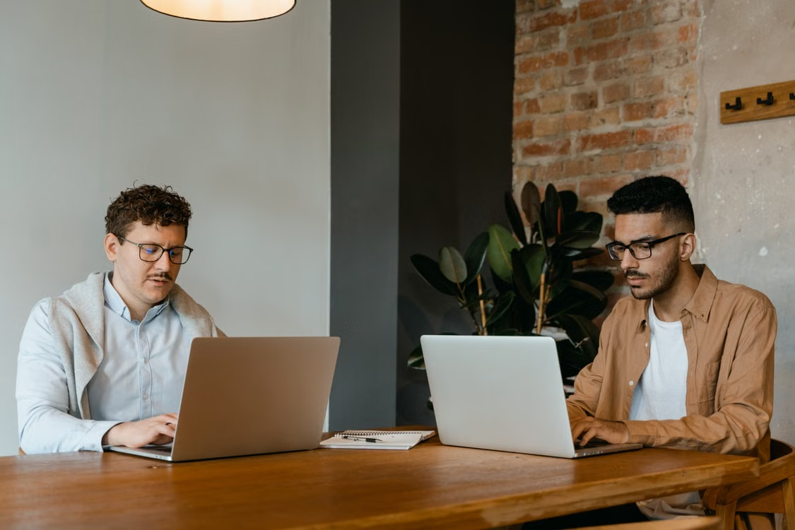 Two software developers working side by side on laptops, illustrating collaborative nearshore software development.
