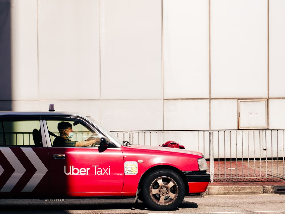 Red Uber Taxi parked beside a city sidewalk, with a driver visible inside.