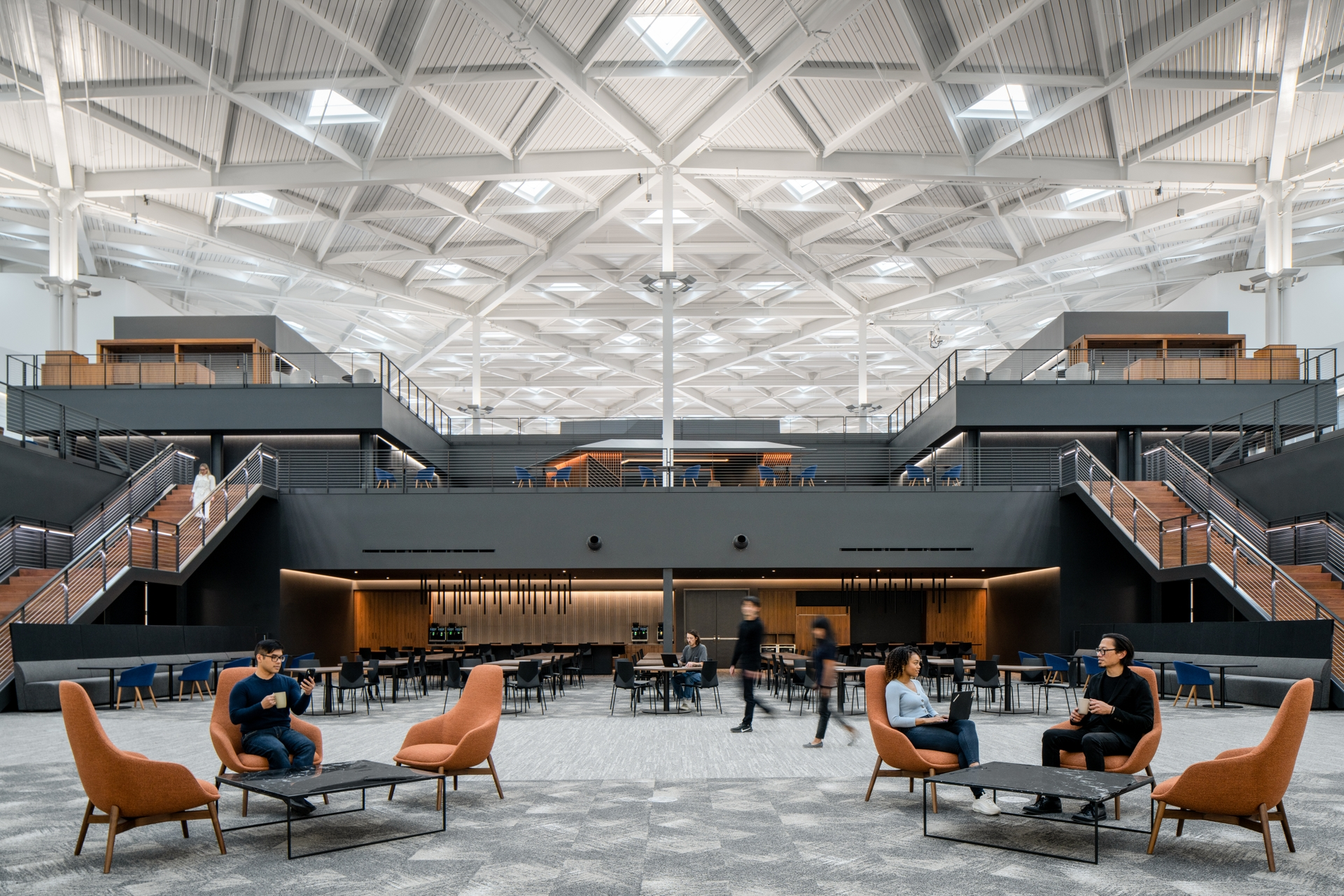 Interior of NVIDIA’s Voyager headquarters in Santa Clara, showing a large open atrium with skylights, mezzanine walkways, staircases, lounge seating, and employees working and talking.