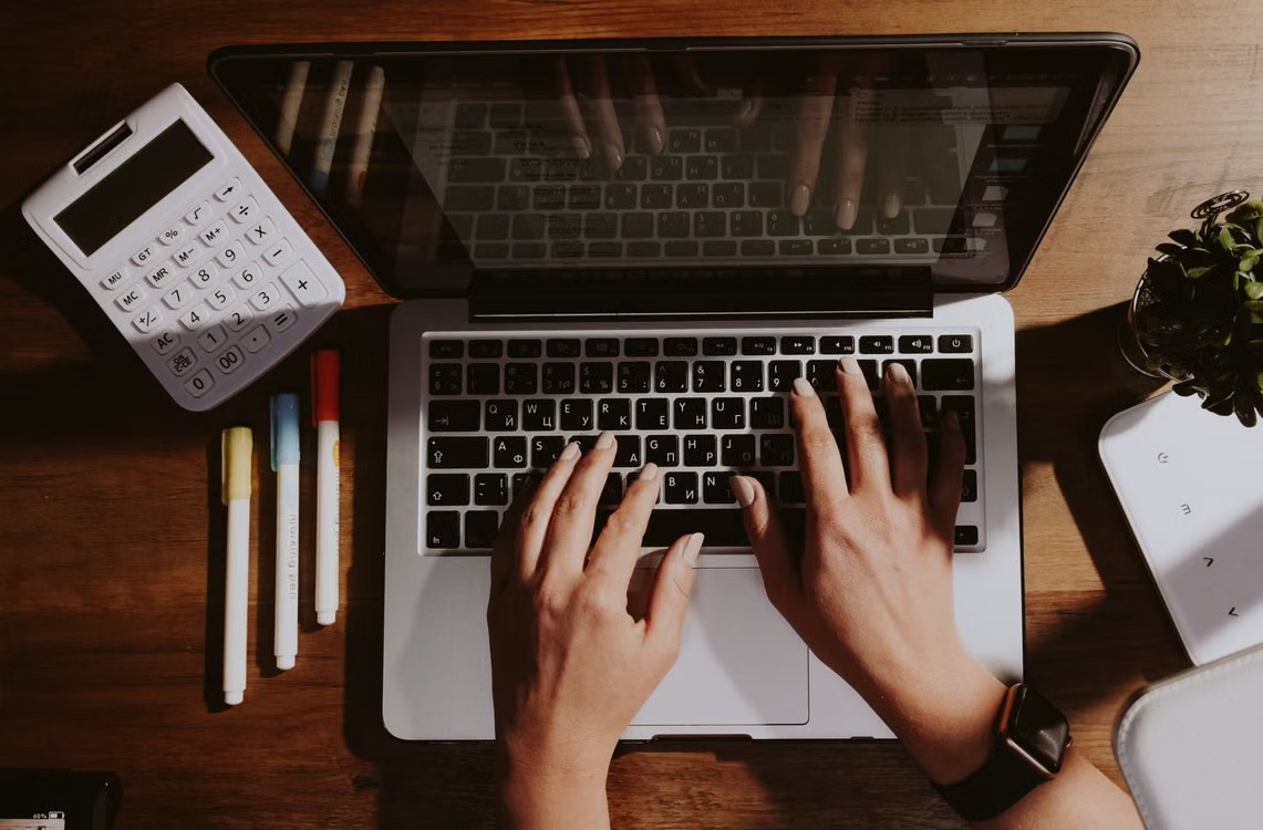 Overhead view of a professional typing on a laptop beside a calculator, illustrating the effort of assessing enterprise AI output, response quality, and hidden costs.