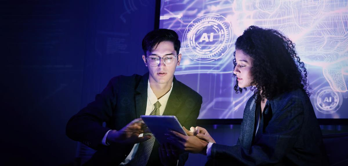Two business professionals reviewing an AI-enabled product on a tablet, with digital artificial intelligence interfaces displayed behind them.