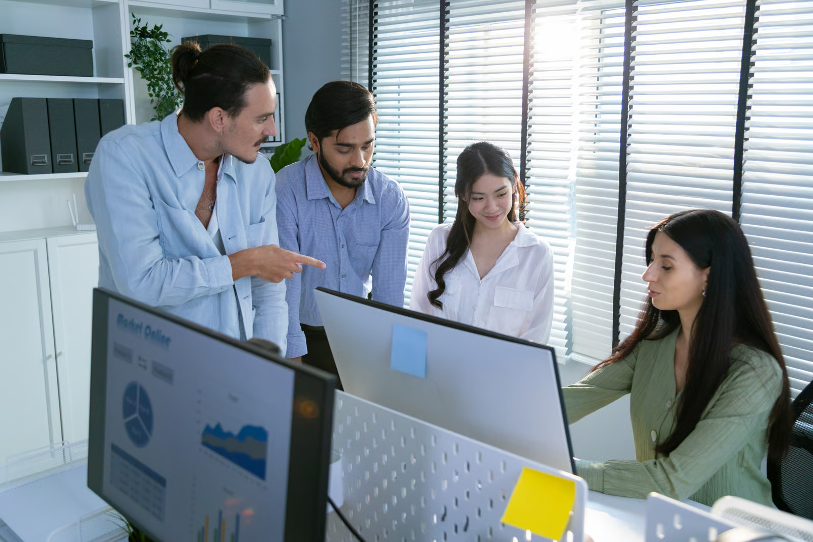 Cross-functional business team reviews dashboards and project data on desktop monitors while planning AI infrastructure and delivery requirements.