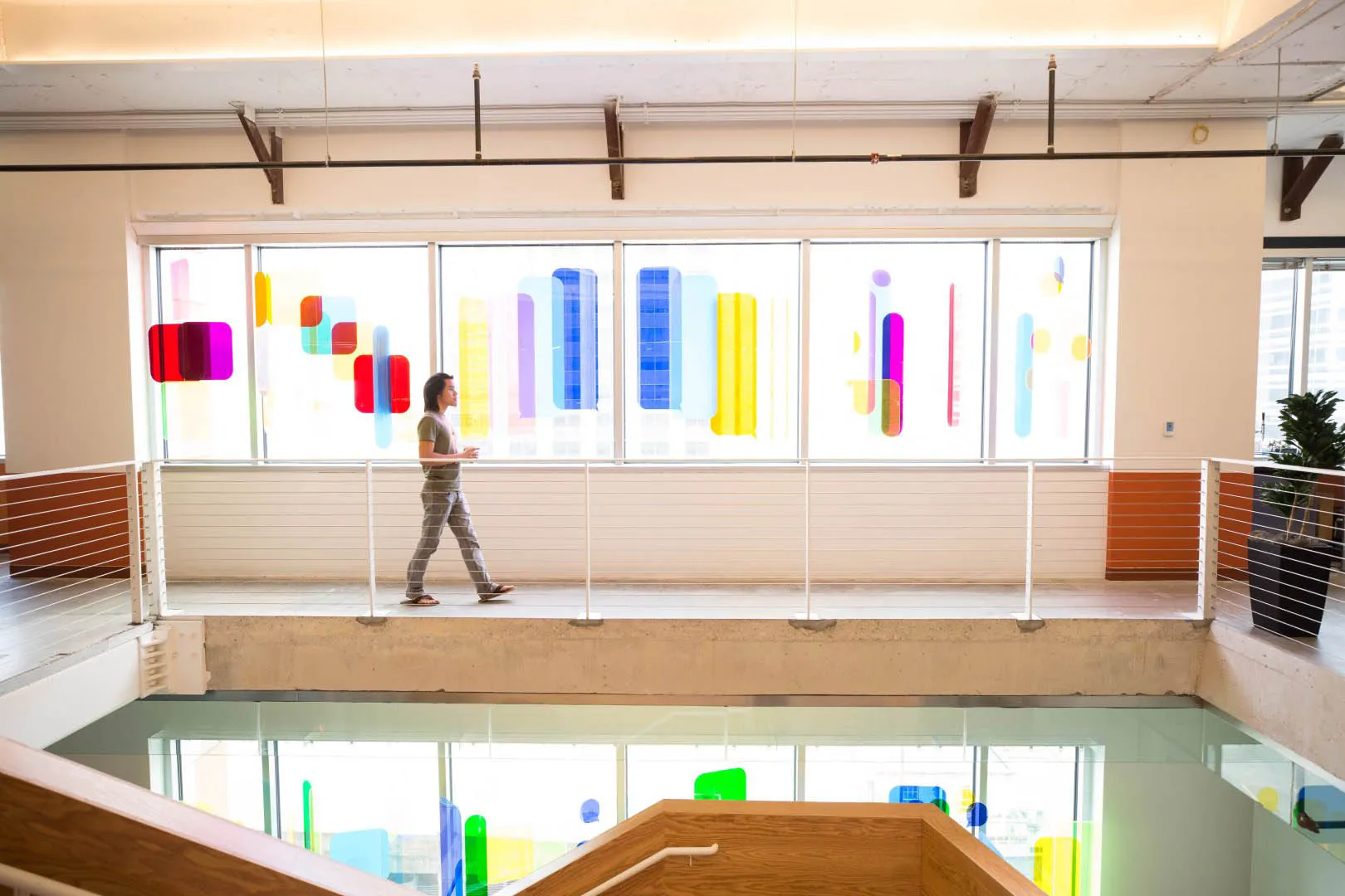 Employee walking through a bright Meta office atrium with colorful geometric window artwork, white railings, and open interior levels. Image courtesy of Meta, 2026.