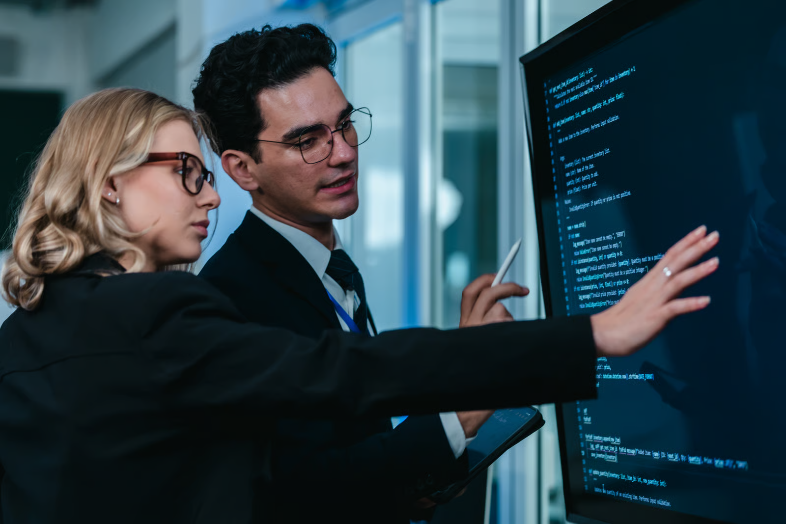 Two professionals review code on a large monitor, illustrating collaborative human oversight and quality checks for AI-assisted software changes.