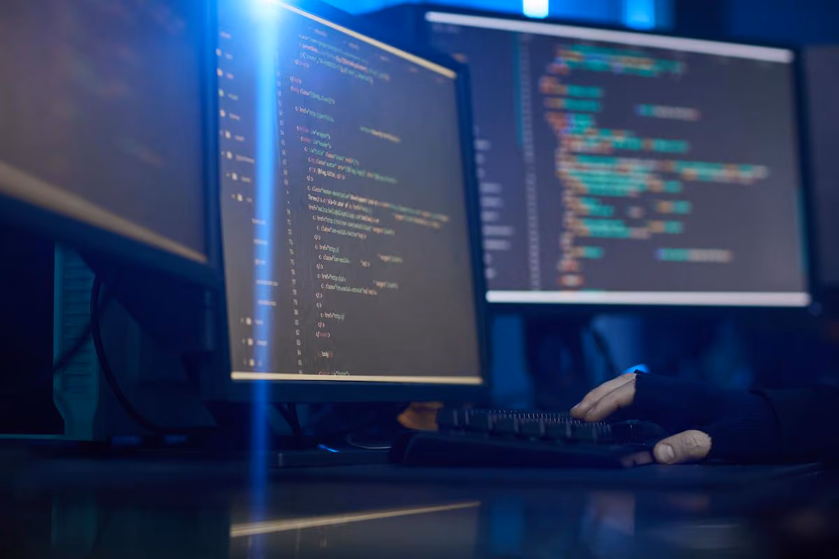 Developer typing at a multi-monitor workstation displaying code, illustrating software development and AI-powered workflows.