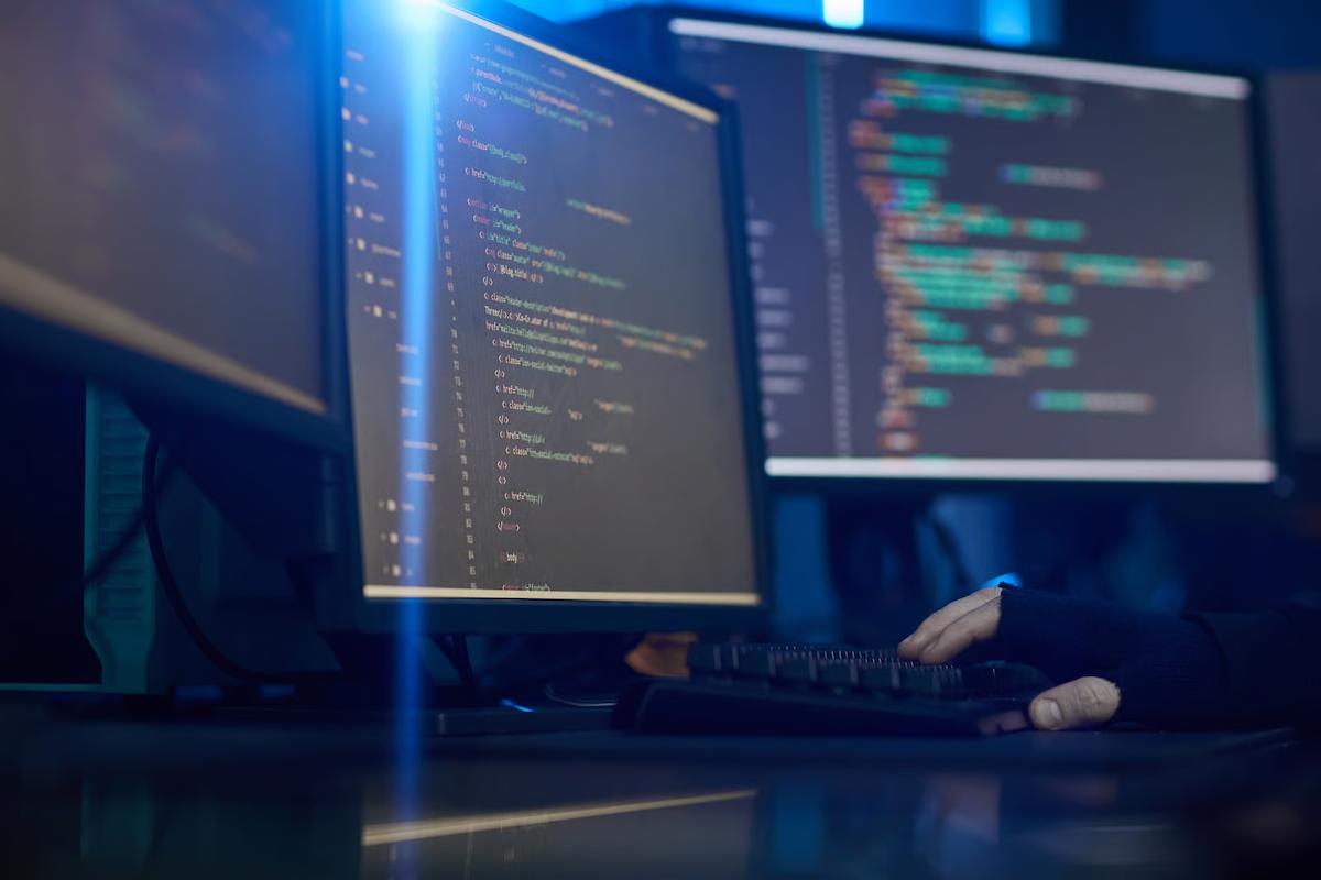 Developer typing at a multi-monitor workstation displaying code, illustrating software development and AI-powered workflows.
