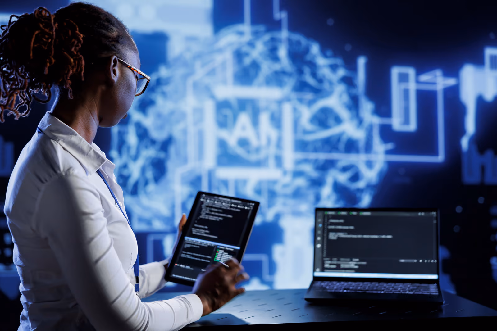 Engineer holding a tablet with code next to a laptop, in front of a glowing blue AI brain graphic, illustrating teams evaluating a Gemini 3.8 Flash upgrade