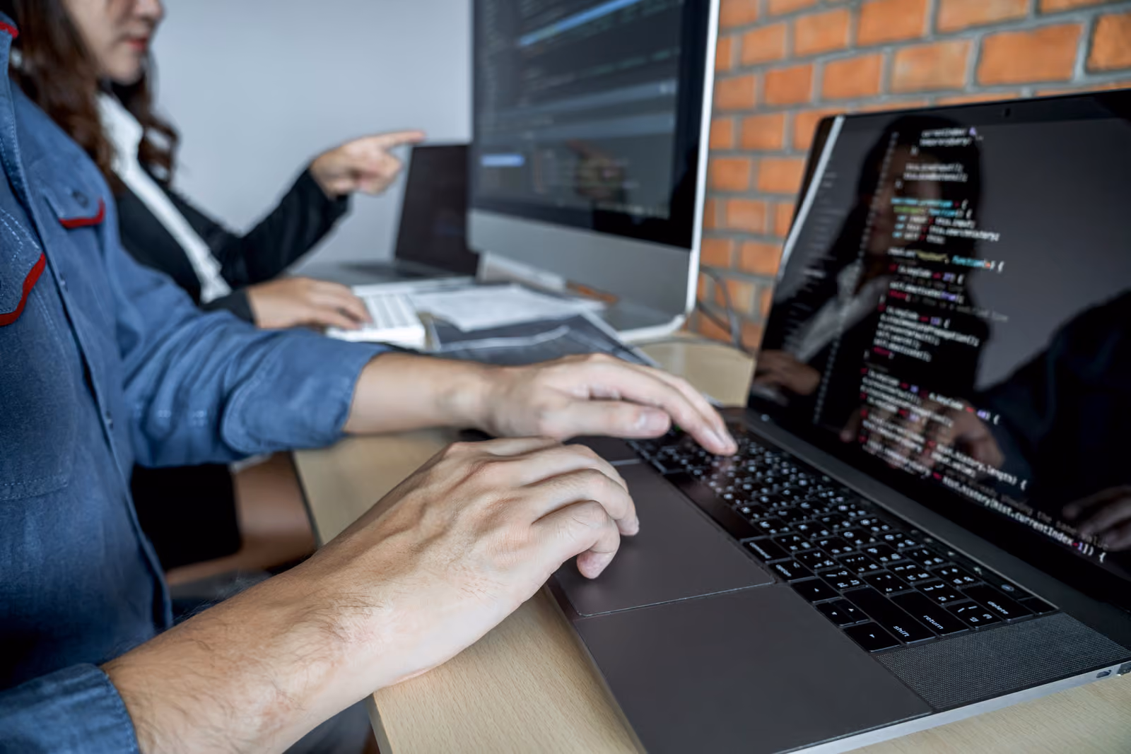 Developer typing code on a laptop while a colleague points at a monitor, illustrating teams evaluating Gemini, Claude, and ChatGPT for enterprise coding and data work