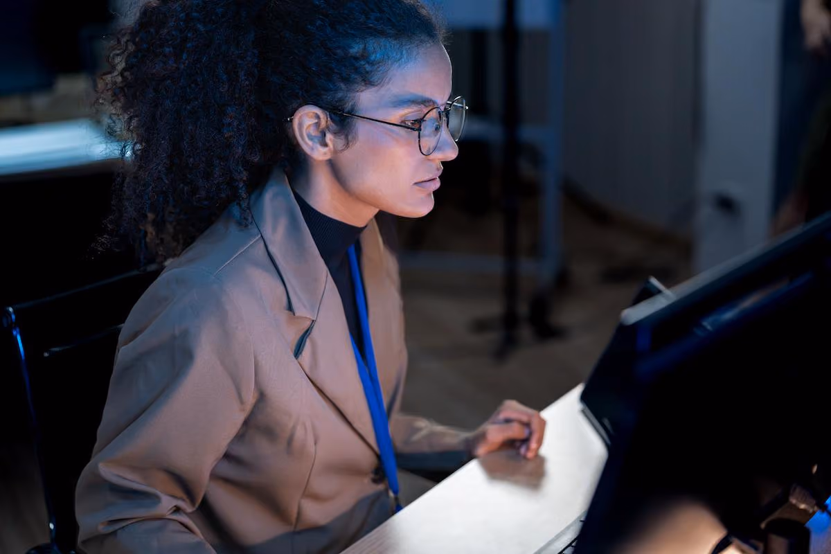 Data professional in glasses focused on a computer monitor in a dimly lit office, illustrating teams building semantic layers so AI agents can use governed business data