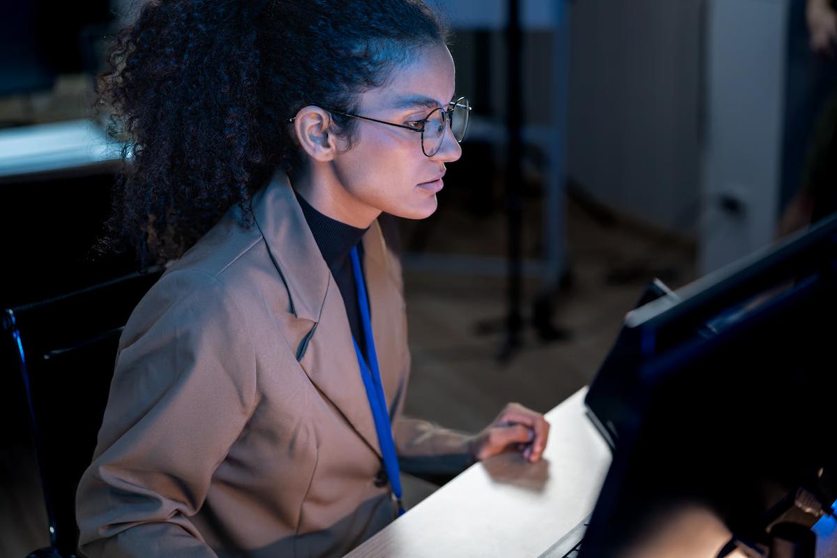 Data professional in glasses focused on a computer monitor in a dimly lit office, illustrating teams building semantic layers so AI agents can use governed business data