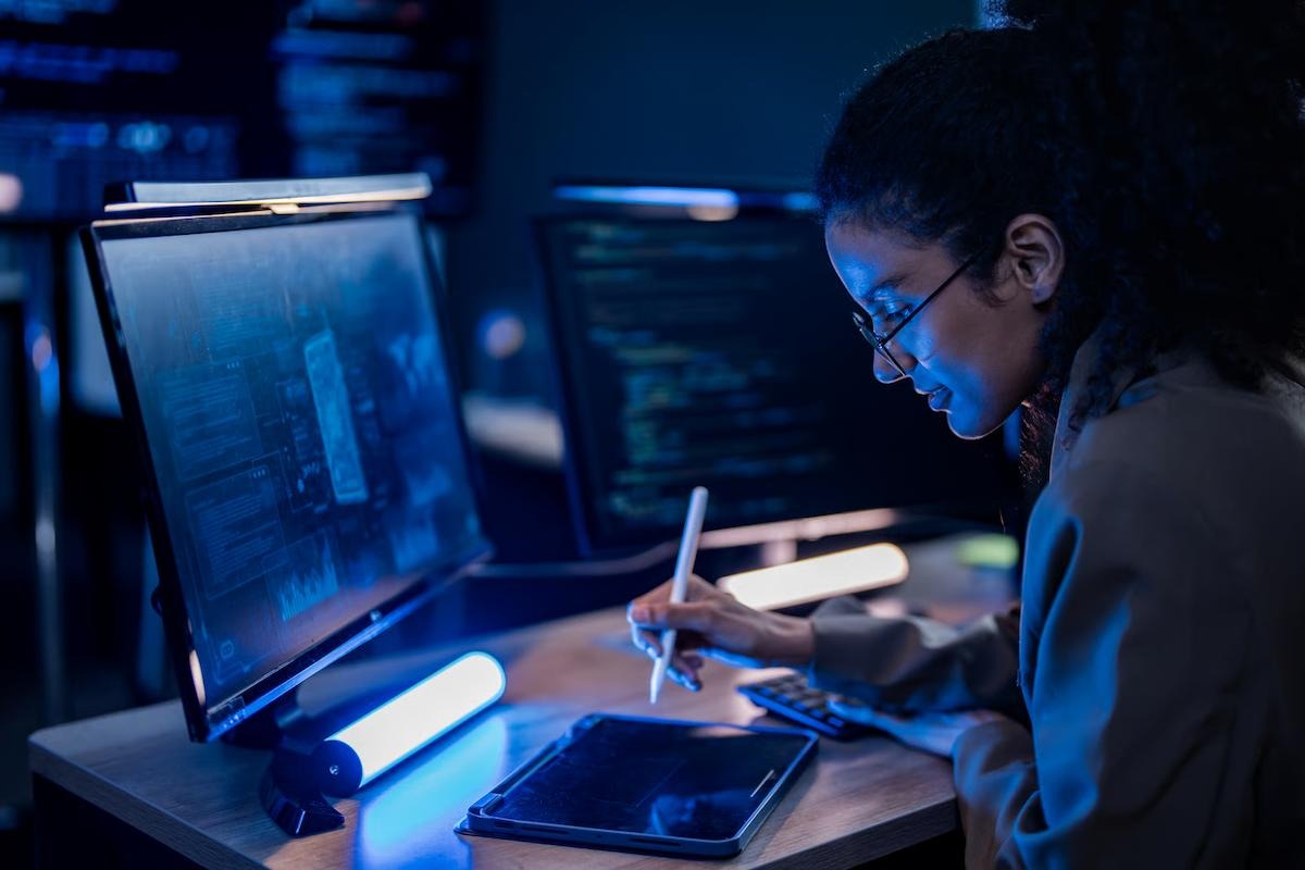 An engineer in glasses takes notes on a tablet with a stylus at a dim, blue-lit desk, with monitors showing data dashboards and code, illustrating a team measuring GPT-6.1 Sol and GPT-6 Sol response times, output speed, and cost per task
