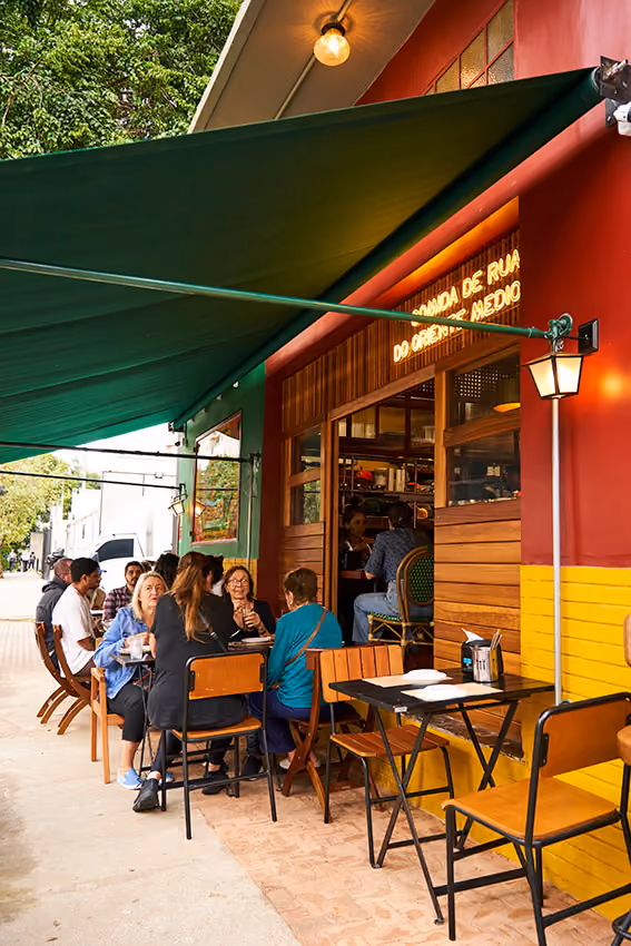 Fachada do Shuk de dia, com toldo verde e mesas na calçada