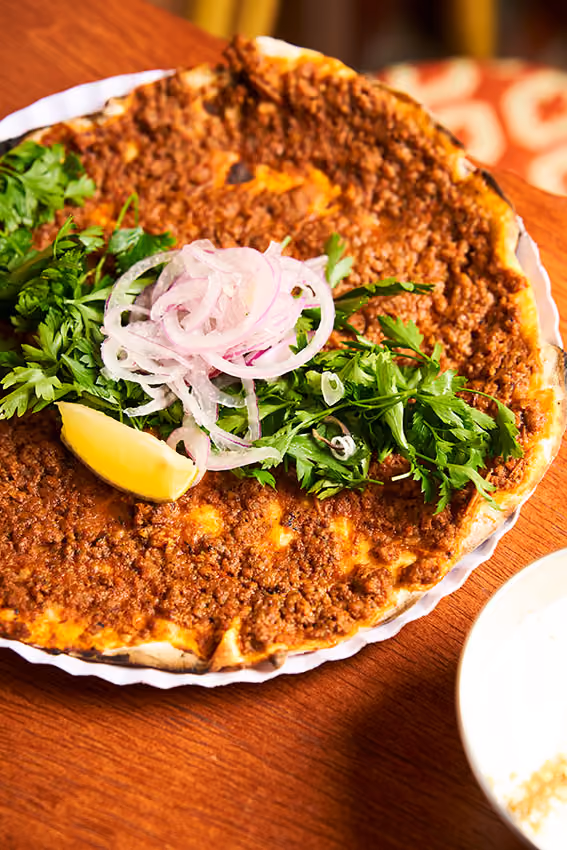 Lahmacun coberto com carne moída, cebola fatiada, salsa fresca e uma rodela de limão.