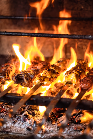 Espetos de kebab assando na brasa, entre chamas altas
