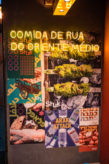 Neon amarelo com a frase comida de rua do Oriente Médio sobre uma parede de pôsteres do Shuk