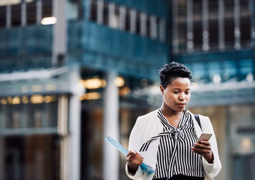 A short-haired woman in professional business attire calls an attorney after leaving her office building in the background.