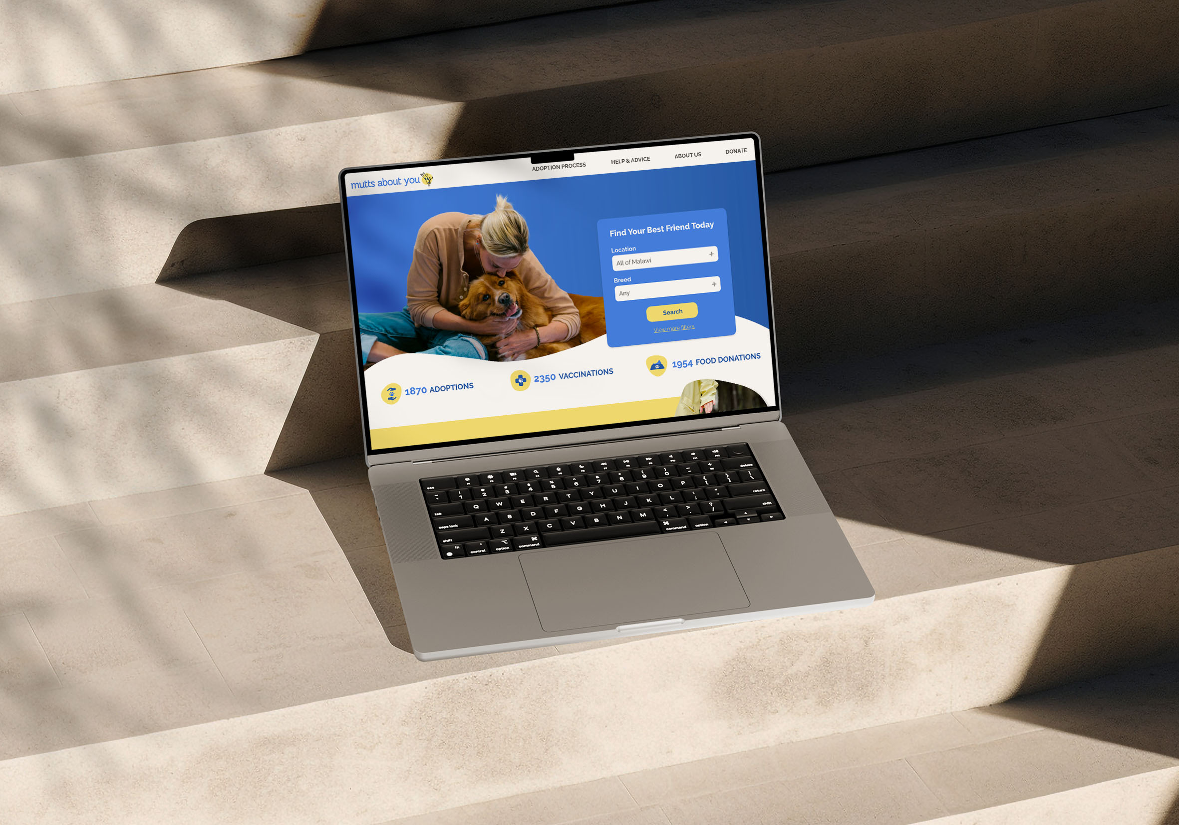Silver Macbook laying on steps, showing the homepage of a dog adoption website