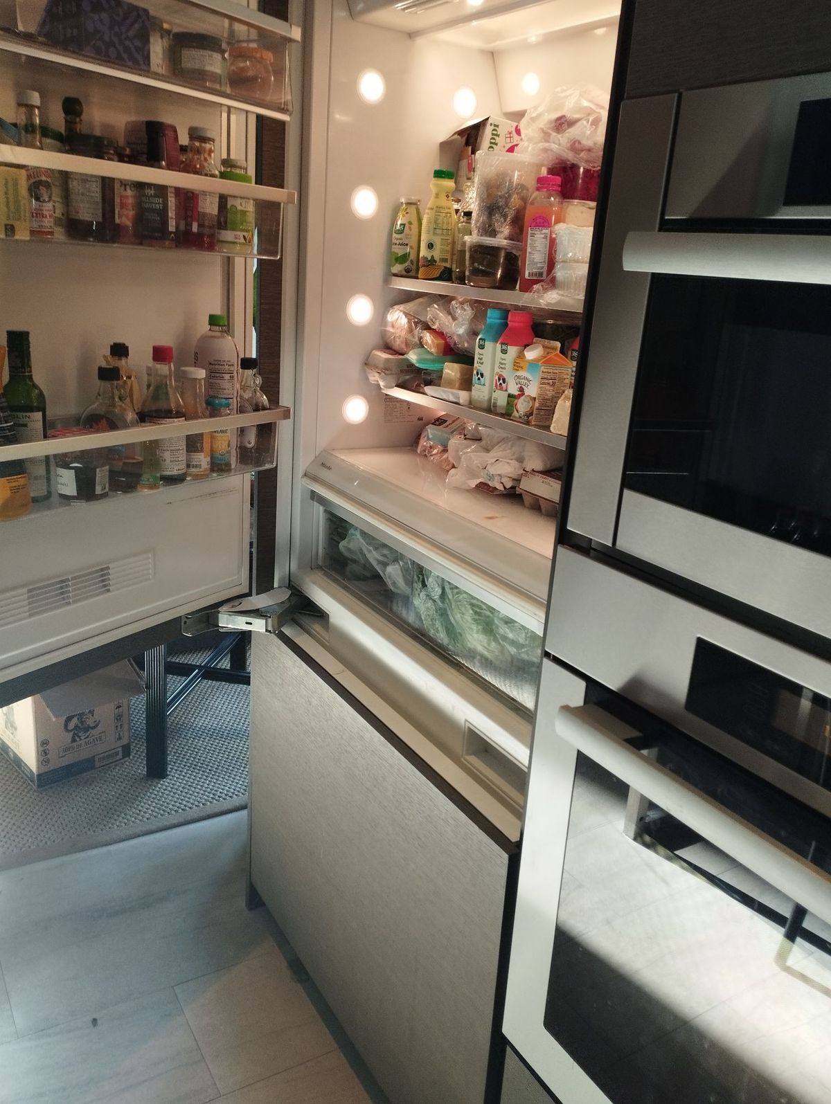 Built-in Miele refrigerator with door open in a NYC kitchen, built-in wall ovens beside it