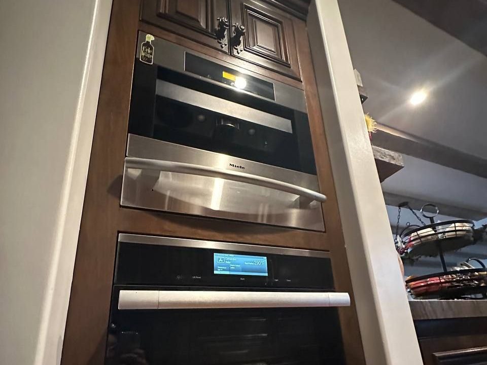 Miele built-in appliance tower in a NYC apartment: coffee machine, warming drawer and steam oven in dark wood cabinetry